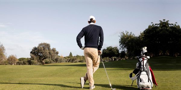 Golfer steht entspannt mit dem Rücken zum Fotografen und Blickt in die Ferne. Neben ihm steht das Golfbag.