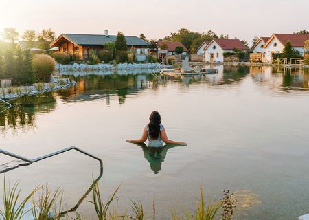 Eine Frau steht hüfttief im Gartensee. Im Hintergrund sind mehrere Chalets und Bäume zu sehen.