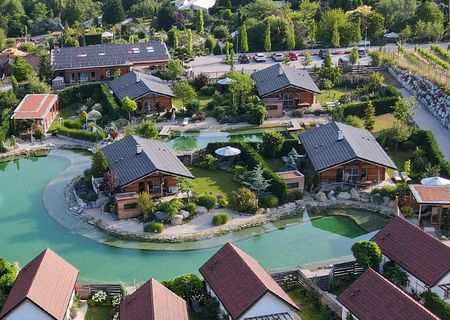 Vogelperspketive auf die Landhäuser der Chalets am Gartensee mit üppiger Begrünung und strahlend blauem See.