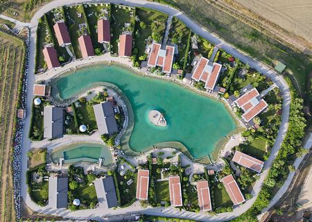Vogelperspketive auf das Areal der Chalets am Gartensee mit üppiger Begrünung und strahlend blauem See.