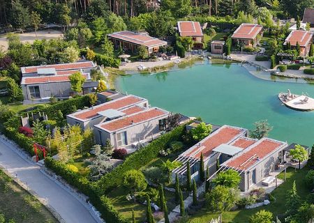 Vogelperspketive auf die Villas der Chalets am Gartensee mit üppiger Begrünung und strahlend blauem See.